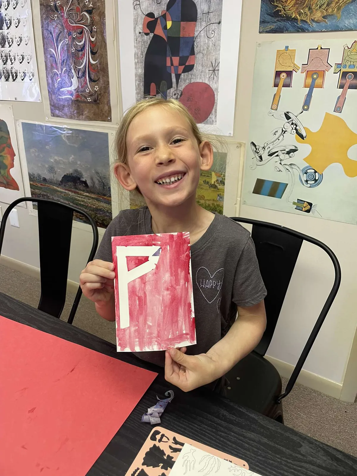 A student holding up her finished red stencil print in front of the art history posters at InDreams Art Experience in Medford, NJ